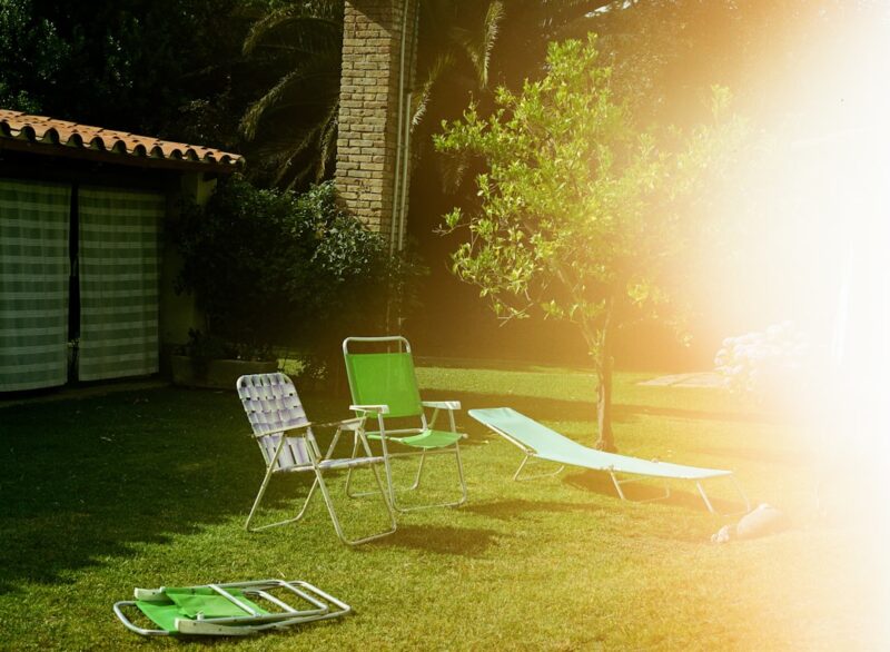 Lawn chairs and lounge on green grass near house.