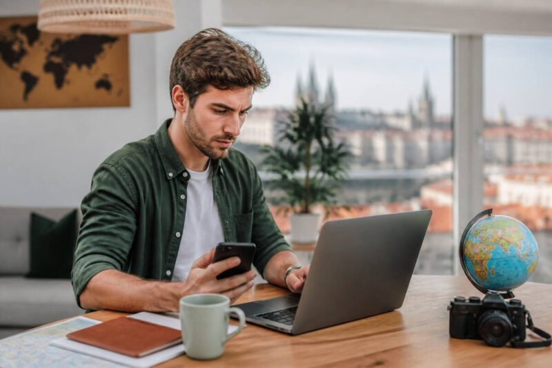 Iemand vergelijkt vakanties op een laptop met notities op tafel